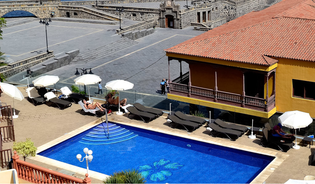 Sun loungers and umbrellas by a pool, yellow building in Garachico, Tenerife.
