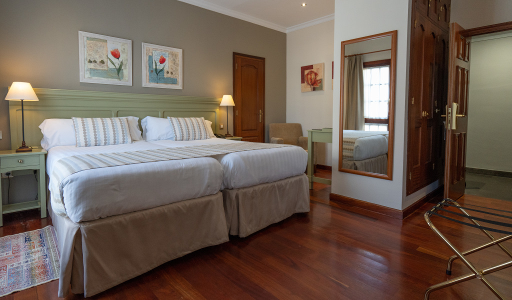 Double bed with pillows in a hotel room in Tenerife, featuring a mirror and wooden floor.