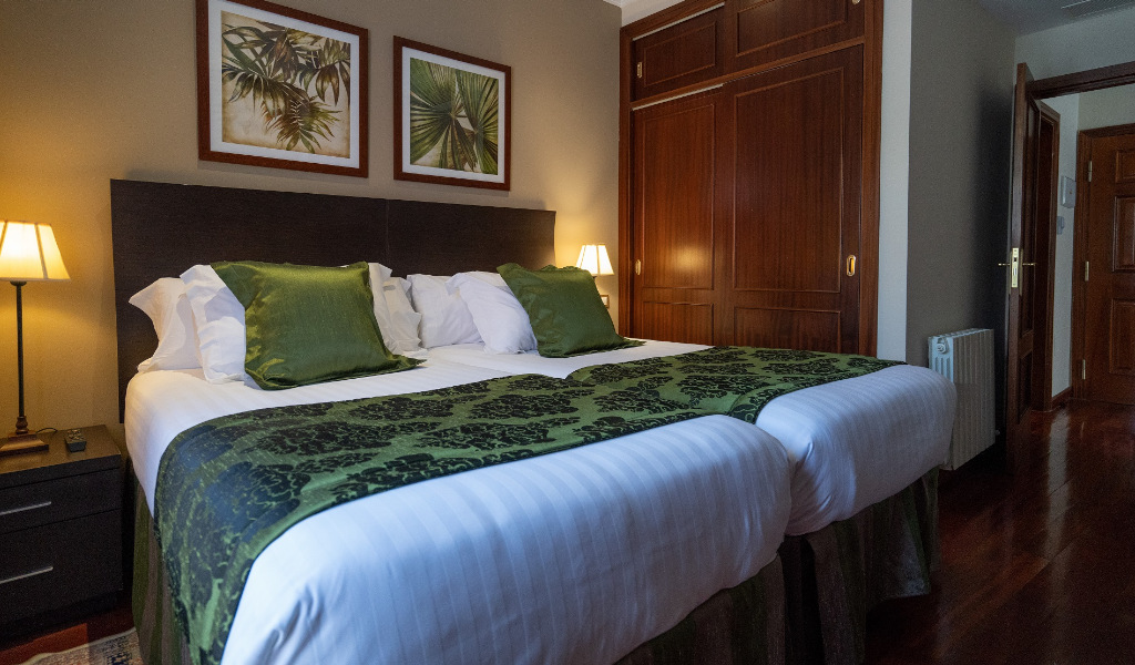 Two twin beds with green pillows and blankets in a Tenerife hotel room.