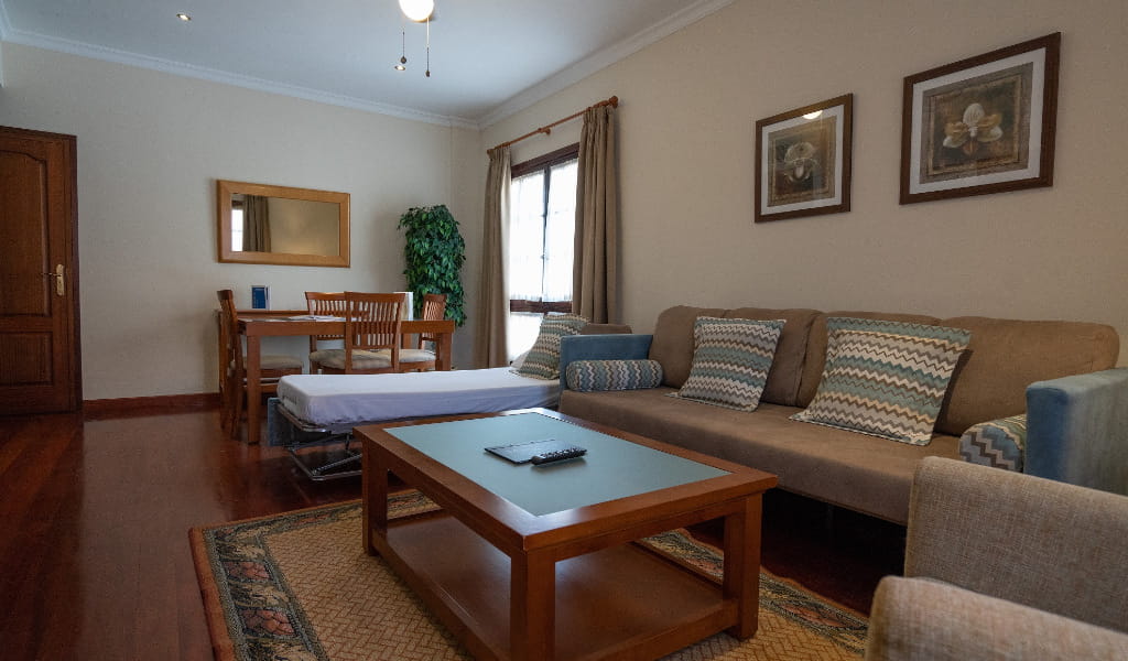 Living room with sofa, coffee table, dining area, and large window in Tenerife apartment.