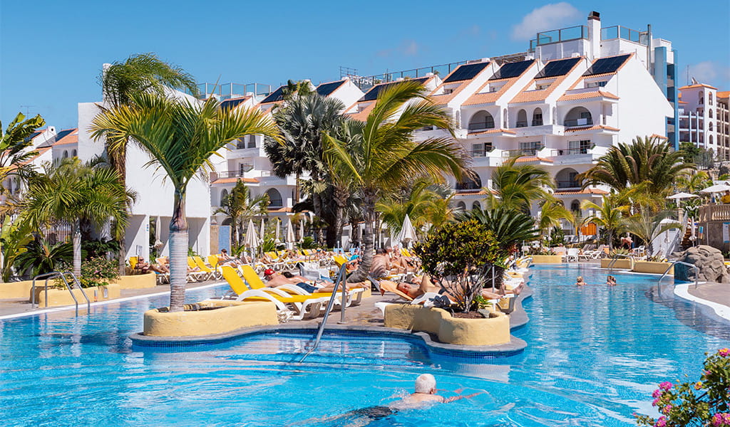 Outdoor pool area with palm trees and sun loungers at a resort in Tenerife.