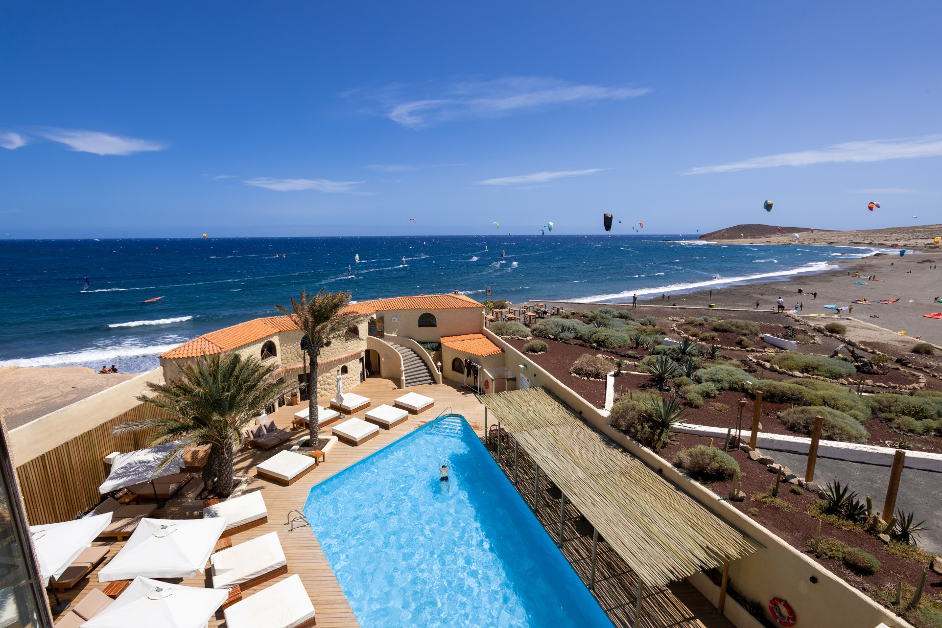 View of El Médano beach in Tenerife with kitesurfers, pool and nearby terrace.