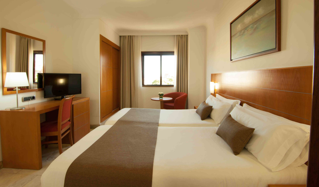 Two beds in a hotel room with a desk and television in Tenerife.
