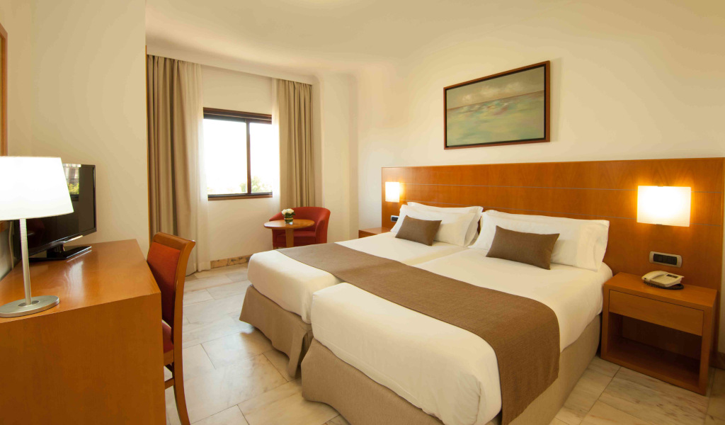 Twin beds in a hotel room with a desk and a window in Tenerife.