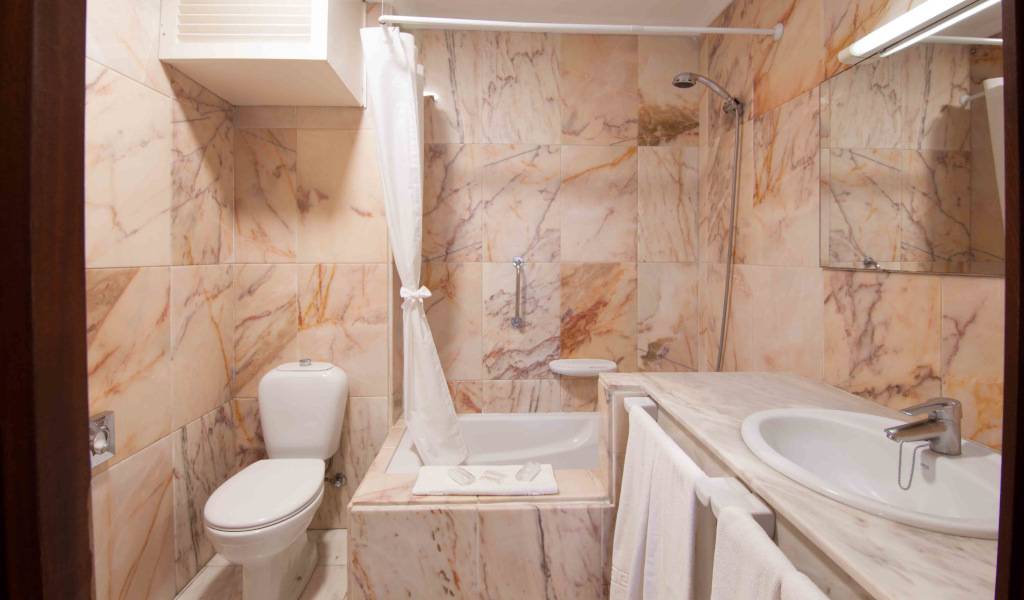 Bathroom with marble tiles, toilet, shower, sink, and mirror in a Tenerife hotel.