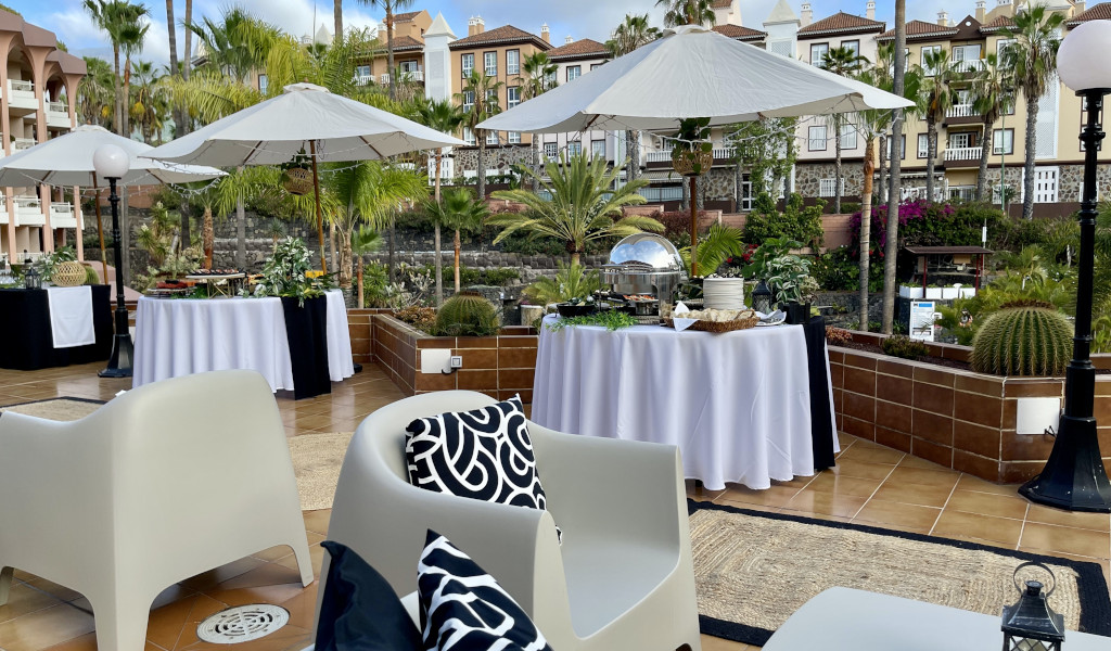 Outdoor event setup with tables and umbrellas in Tenerife garden.
