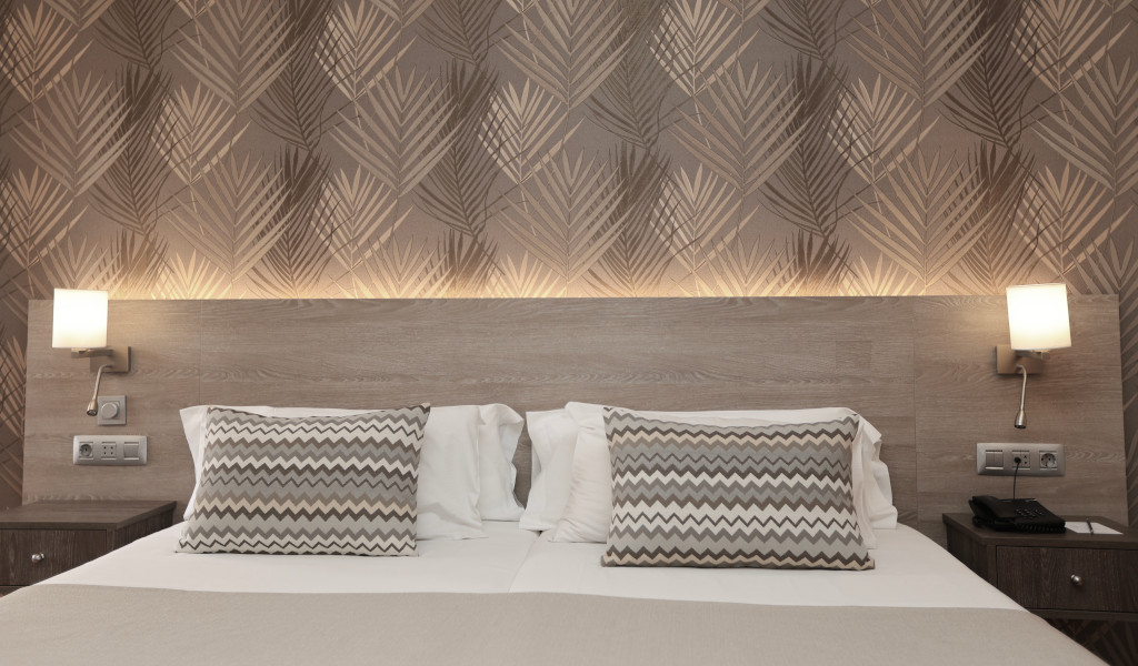 Hotel room bed with patterned pillows and wall lights in Tenerife.