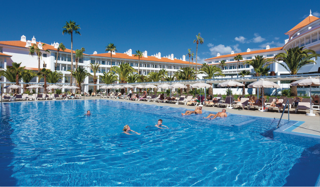 Outdoor swimming pool with people swimming in front of a hotel in Tenerife.