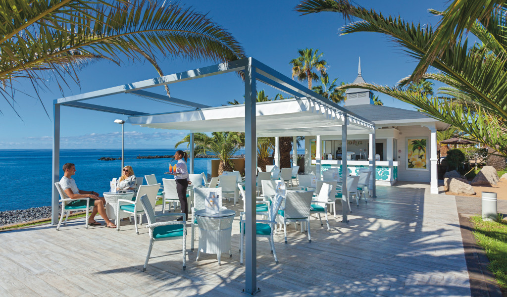 Outdoor café near the sea with people sitting, waiter serving drinks in Tenerife.