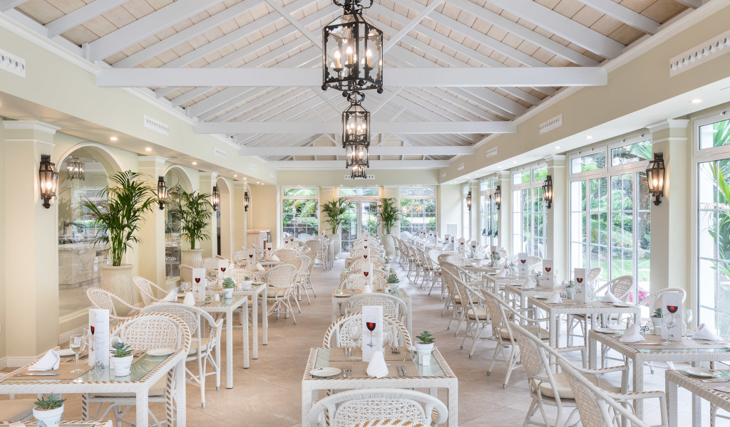 Dining area with white tables and chairs, large windows, and green plants in Tenerife.