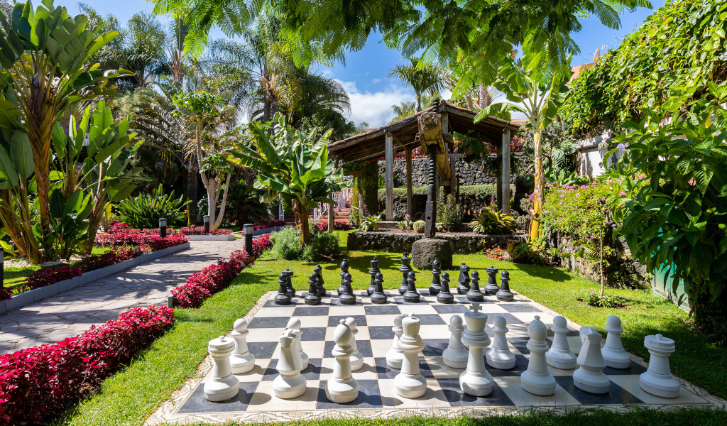 Giant chessboard in a lush garden in Tenerife with tropical plants and a wooden structure.
