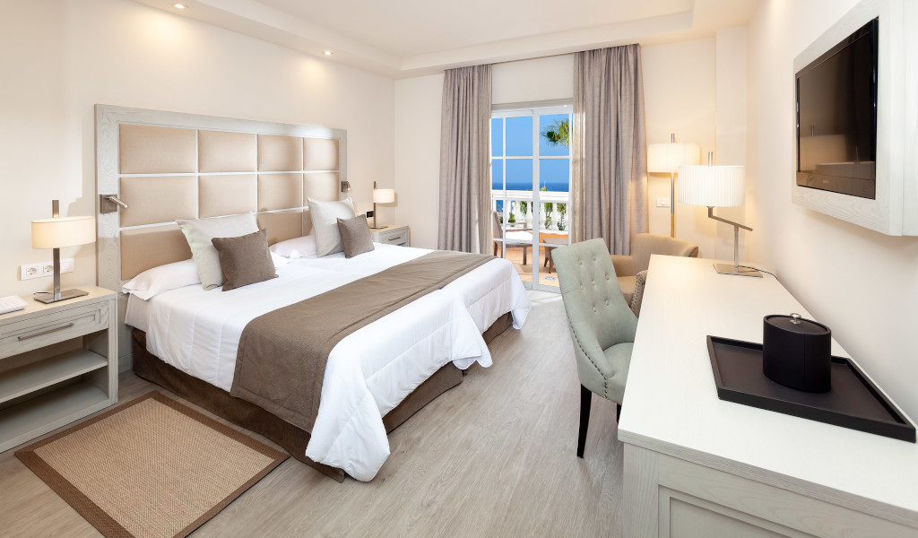 Hotel room with double bed, desk, armchair, and window view of the ocean in Tenerife.