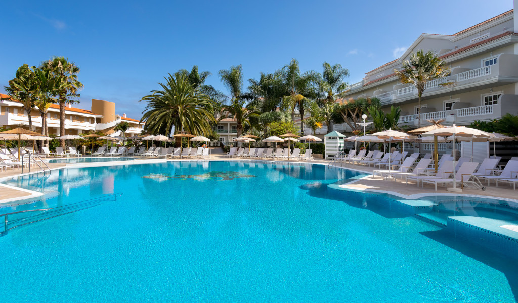 Outdoor pool with palm trees and lounge chairs at a Tenerife hotel.