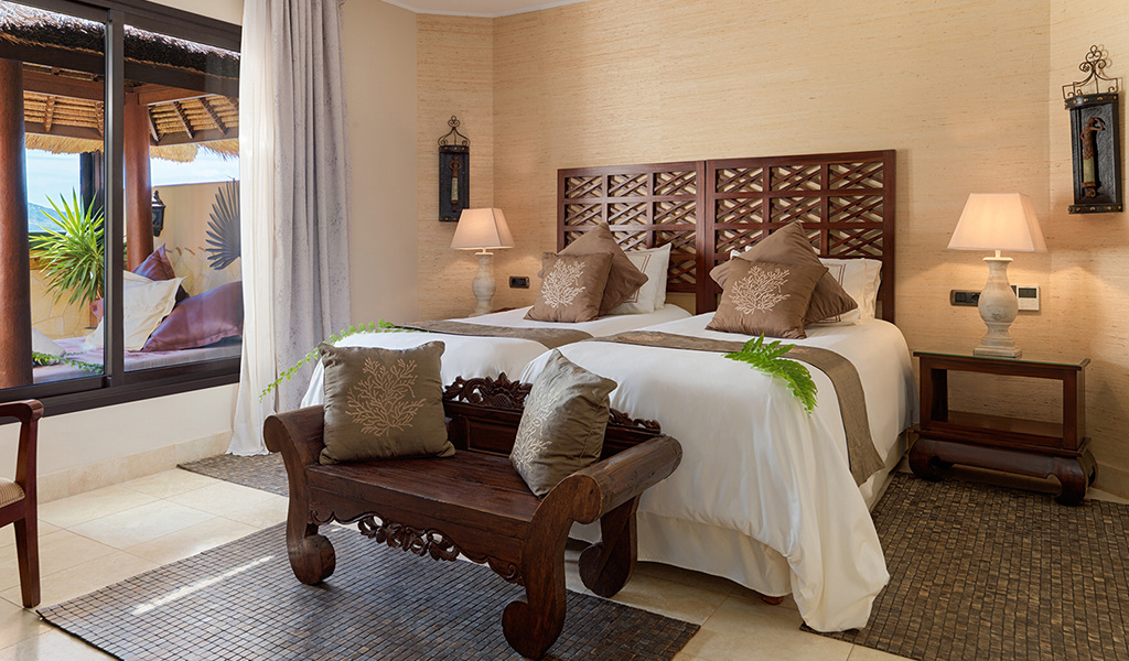 Two beds with decorative pillows and a bench in a hotel room in Tenerife.