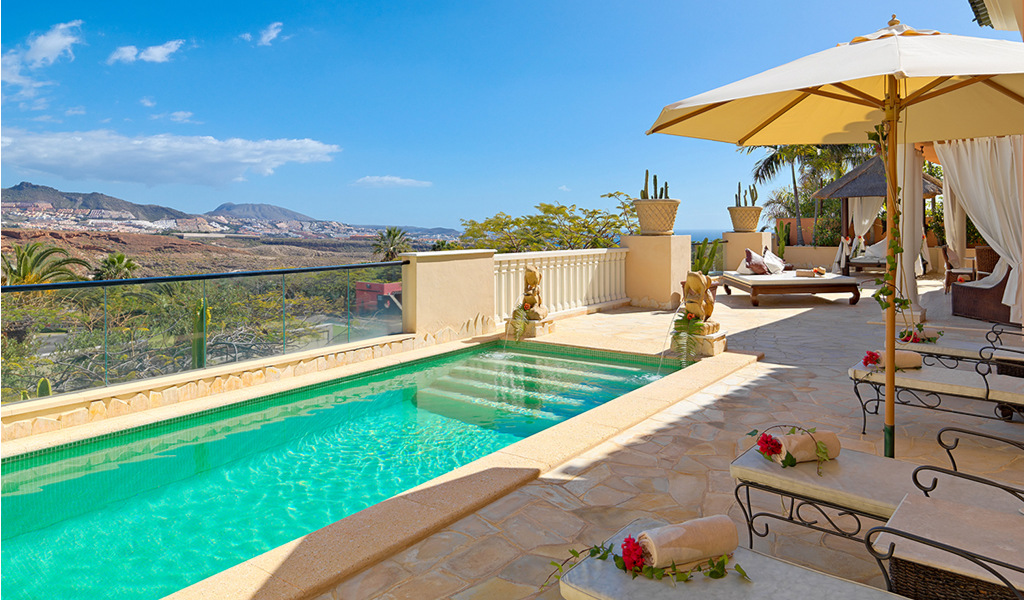 Luxury pool terrace view in Tenerife with sun loungers and parasol.