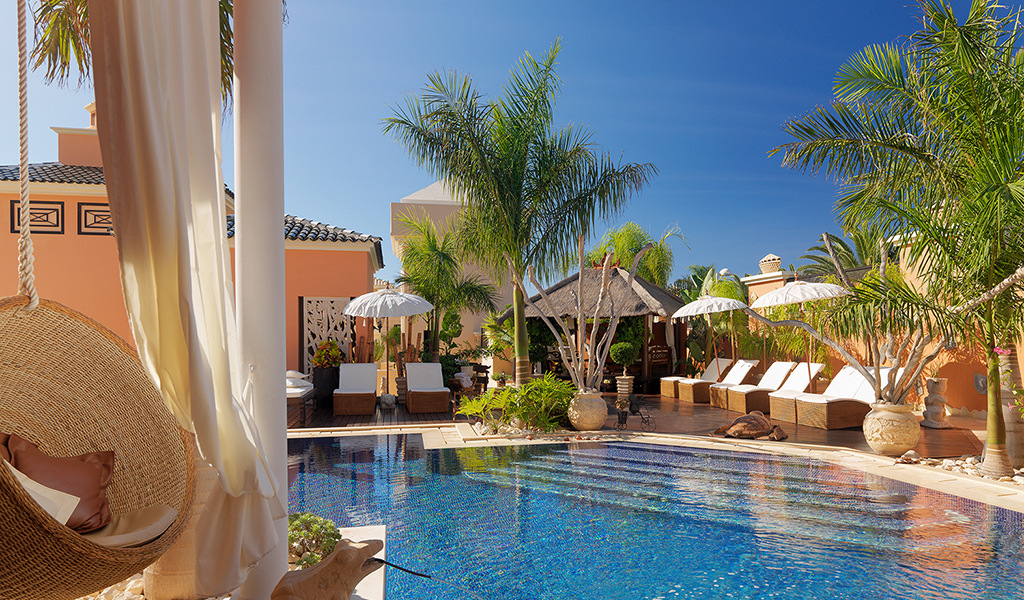 Outdoor pool area with sun loungers, parasols, and palm trees in Tenerife villa.