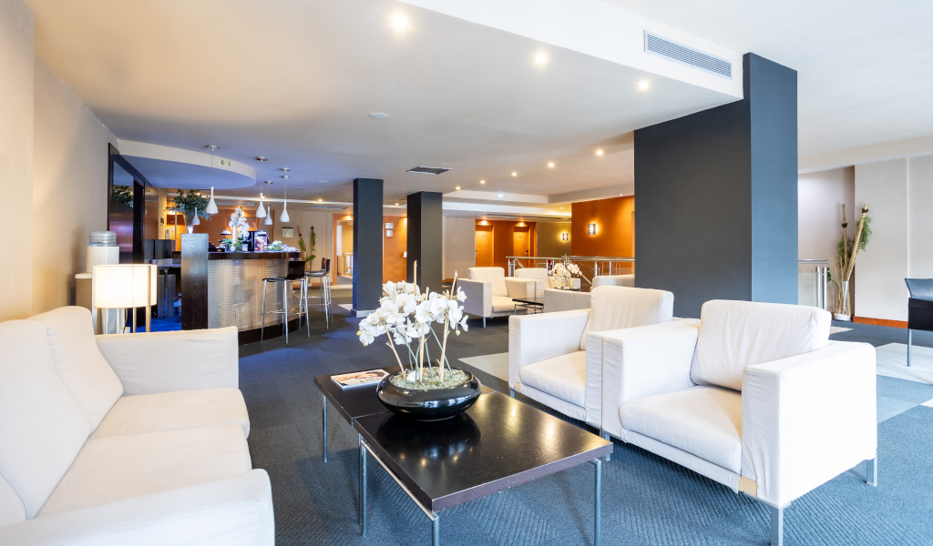 Hotel lounge with white sofas, coffee table with flowers, and a bar in the background in Tenerife.