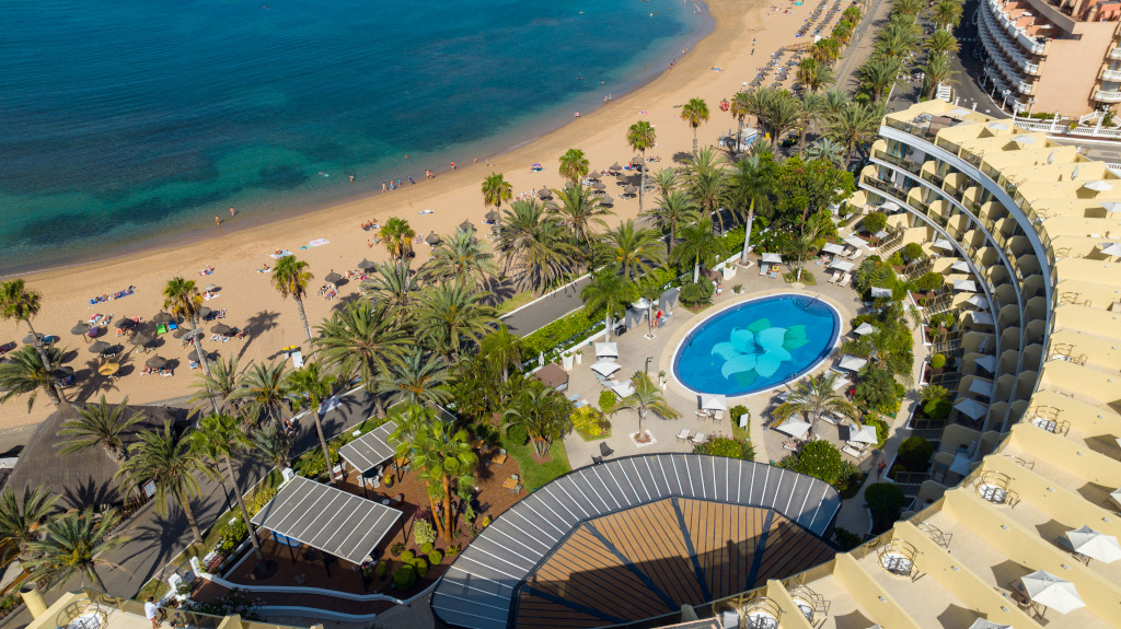 Aerial view of a beach and resort with pool and palm trees in Tenerife.