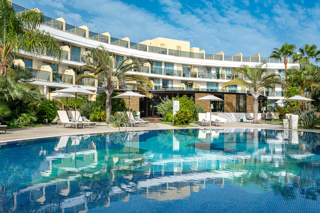 Outdoor pool and sun loungers at a Tenerife resort, surrounded by palm trees.