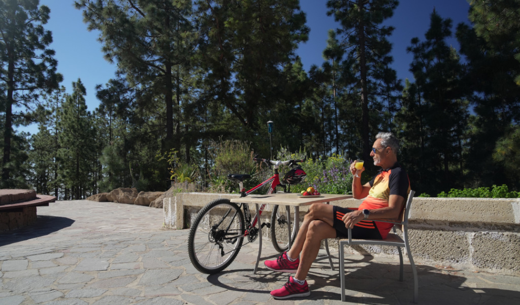 Man enjoying a drink next to a bicycle amid trees in Tenerife.
