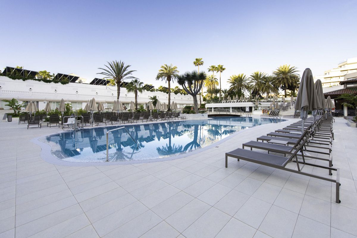 Outdoor swimming pool with sun loungers and palm trees in Tenerife resort.