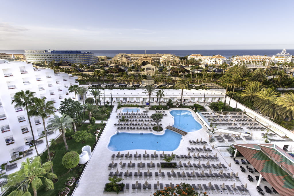 Aerial view of a hotel pool with sun loungers in Tenerife, ocean in the background.