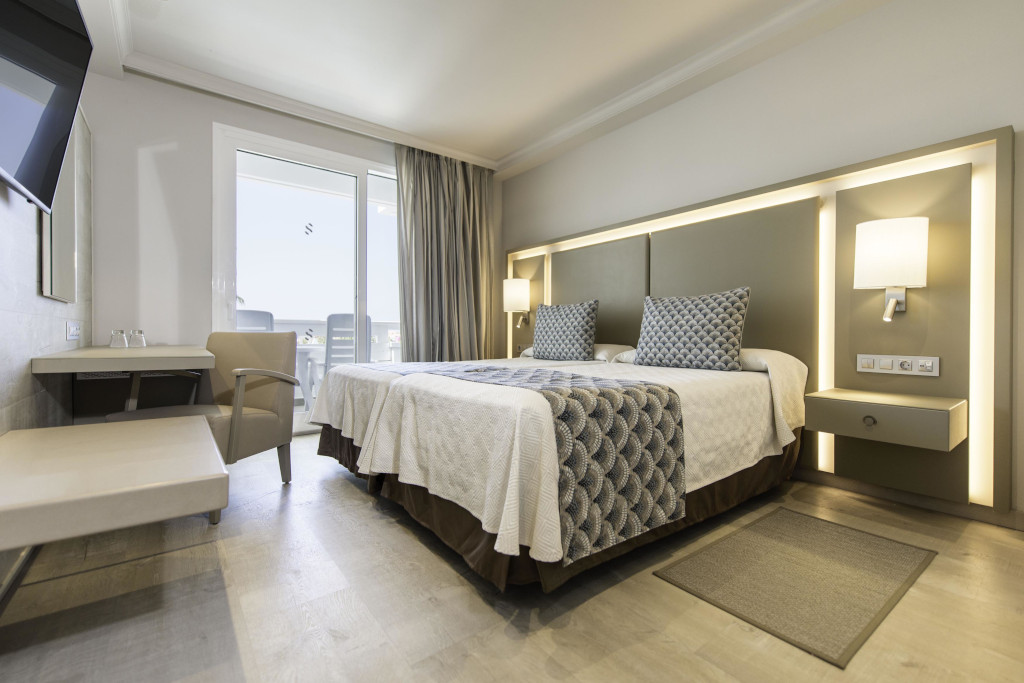 Hotel room in Tenerife with two beds, lamps, armchair, and balcony view.