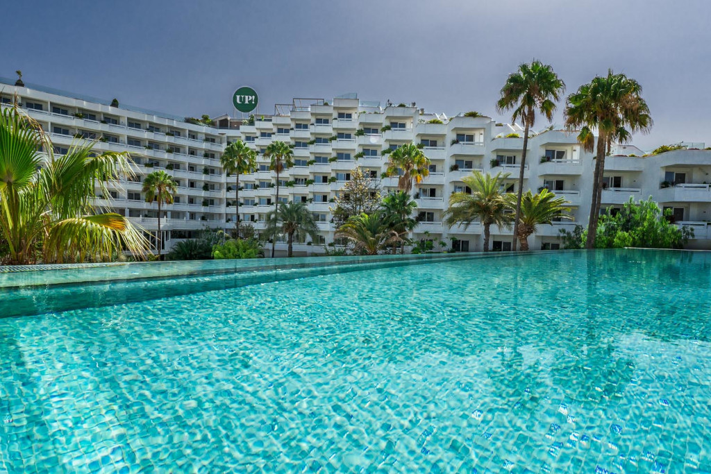Hotel with palm trees and clear pool in Tenerife. Logo on building reads UP!.