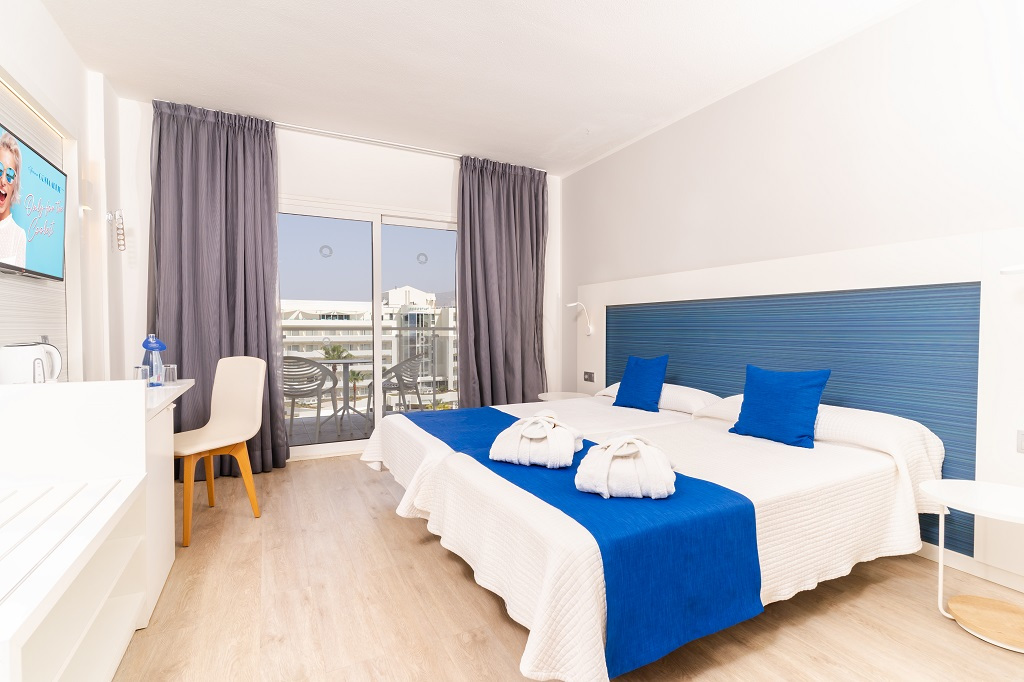 Hotel room in Tenerife with two beds, blue accents, and balcony view.