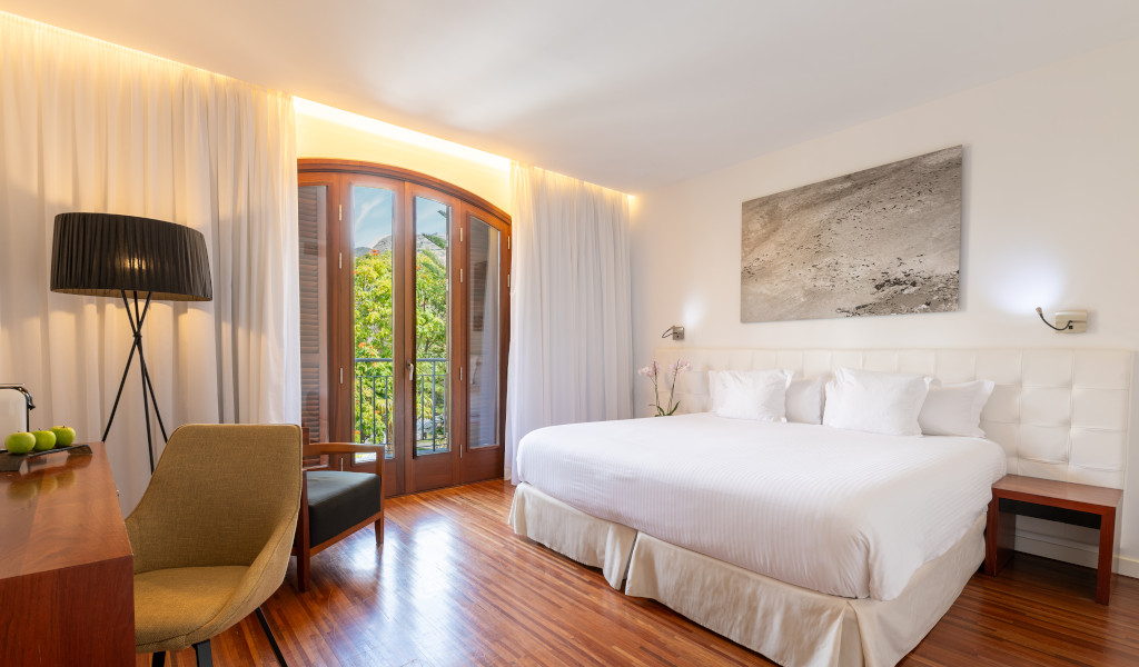 Bedroom with a king-size bed, desk, chair, and window view of trees in Tenerife.