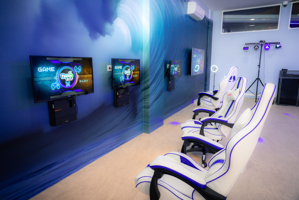 Gaming room in Tenerife with four white chairs and monitors displaying Teens Club.