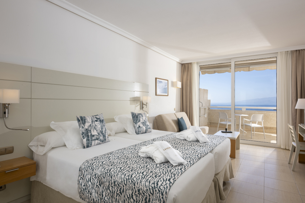 Hotel room in Tenerife with two beds, balcony view, and chairs facing the sea.