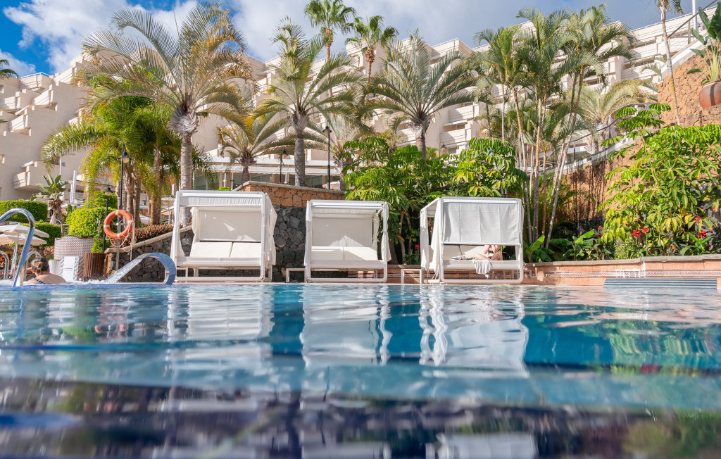 Loungers by the pool surrounded by palm trees in a Tenerife resort.