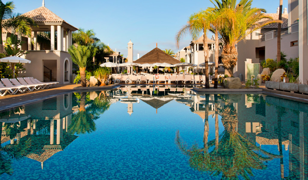 Outdoor pool surrounded by palm trees and sun loungers at a Tenerife resort.