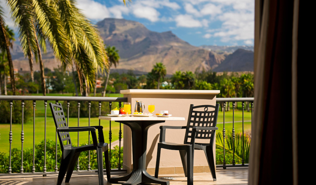 Outdoor dining table with breakfast overlooking Tenerife mountains and palm trees.