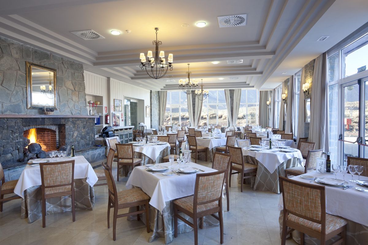 Restaurant dining area with tables set for service, large windows, and stone fireplace in Tenerife.