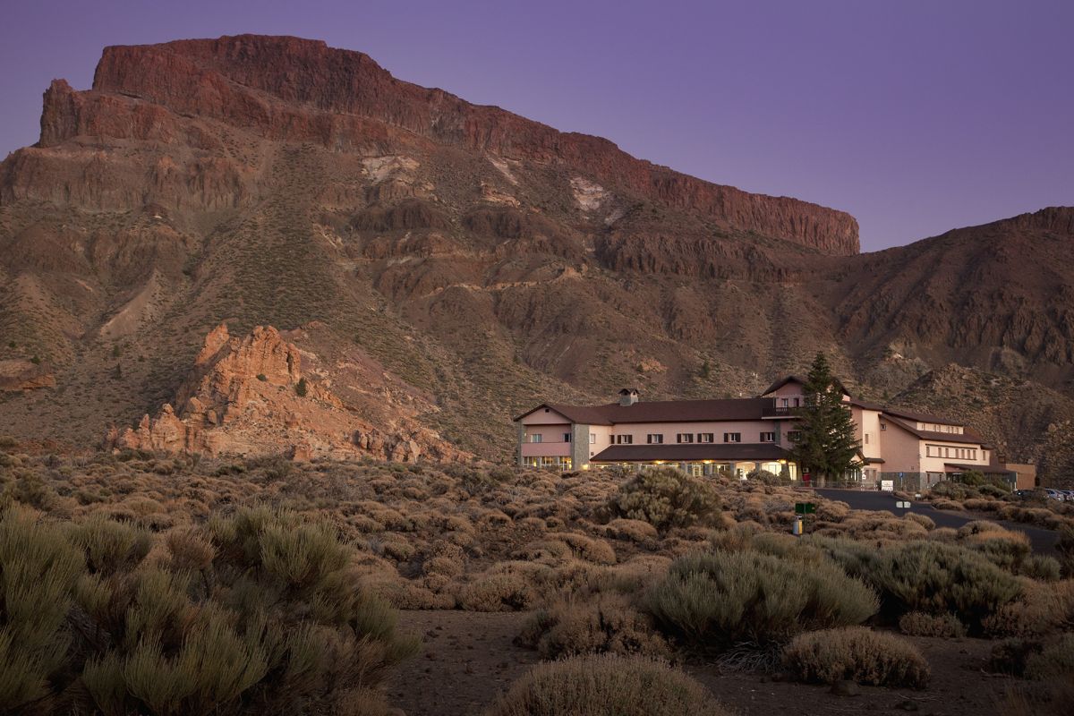 Hotel near volcanic mountain at Teide National Park, Tenerife, under twilight sky.