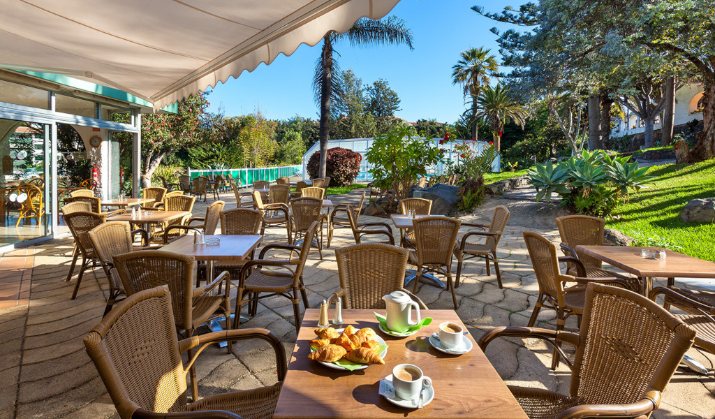 Outdoor cafe with tables and chairs, croissants and coffee, Tenerife garden view.