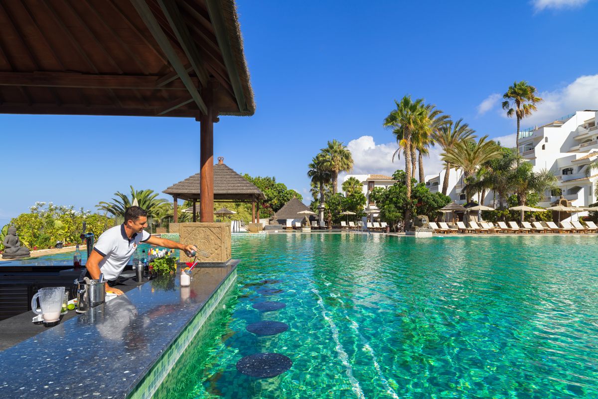 Bartender serving drinks at a poolside bar in a Tenerife resort.