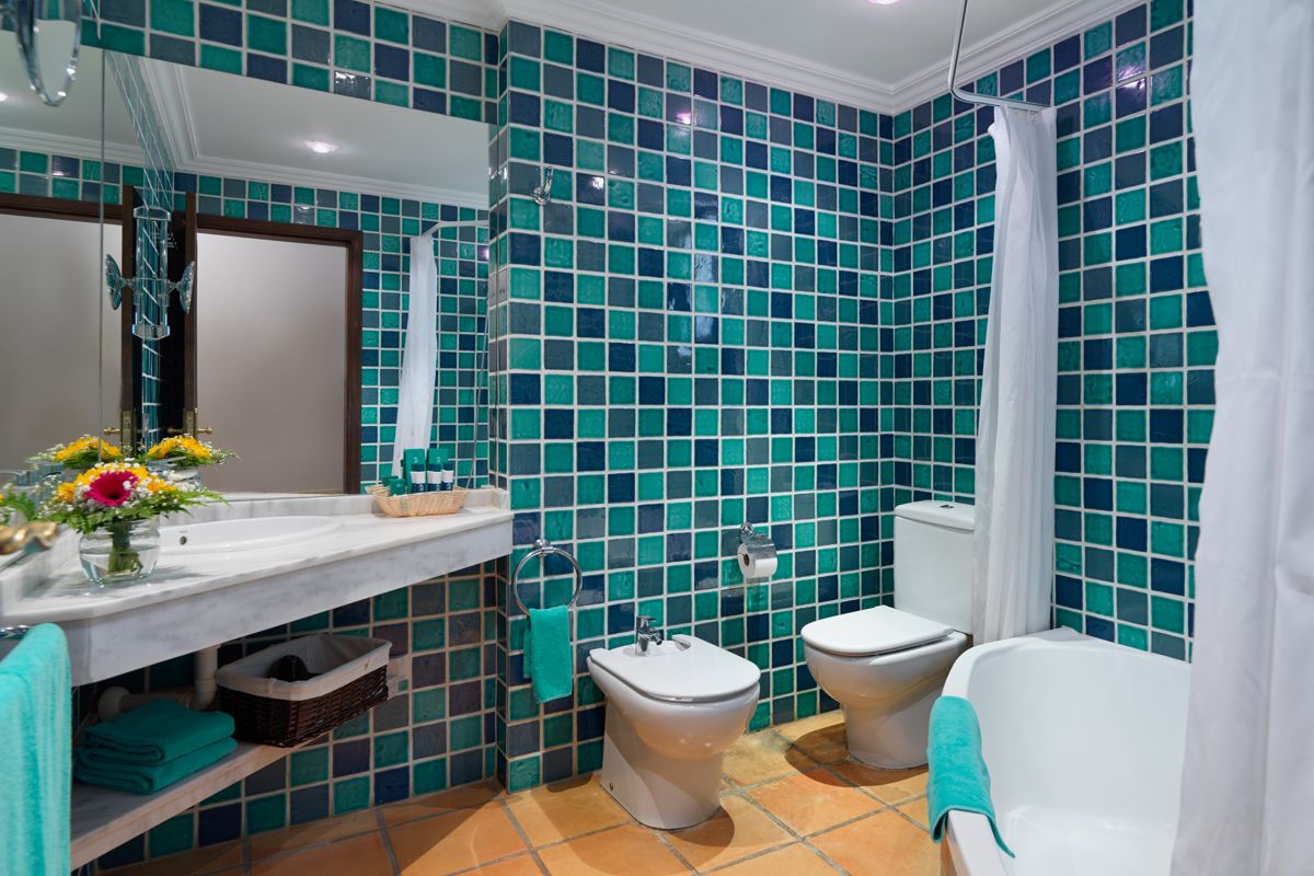 Bathroom with blue-tiled walls, sink, bidet, toilet, and bathtub in Tenerife hotel.