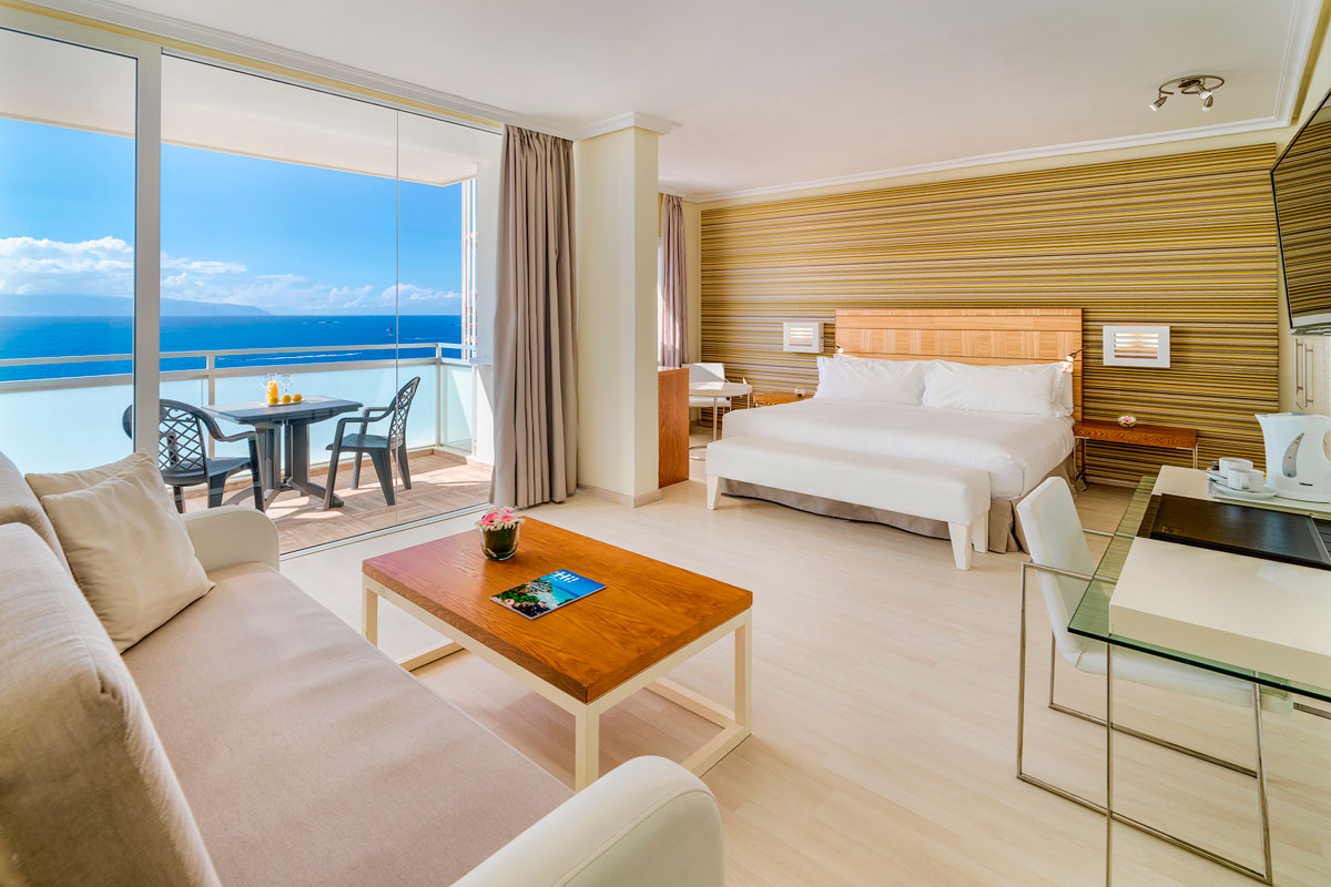 Hotel room with ocean view balcony in Tenerife, featuring a bed, sofa, and table.