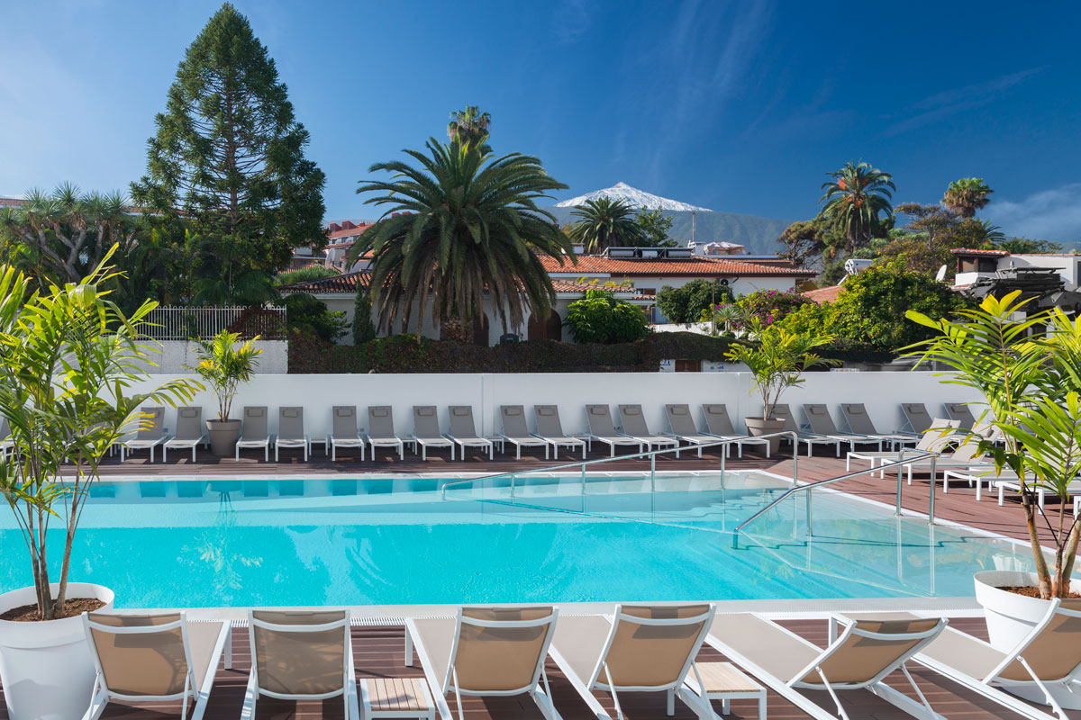 Outdoor pool with lounge chairs and palm trees in Tenerife, with Teide mountain in the background.