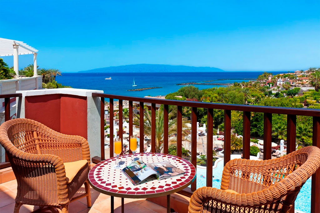 Terrace view of the ocean and La Caleta in Tenerife with a table and chairs.