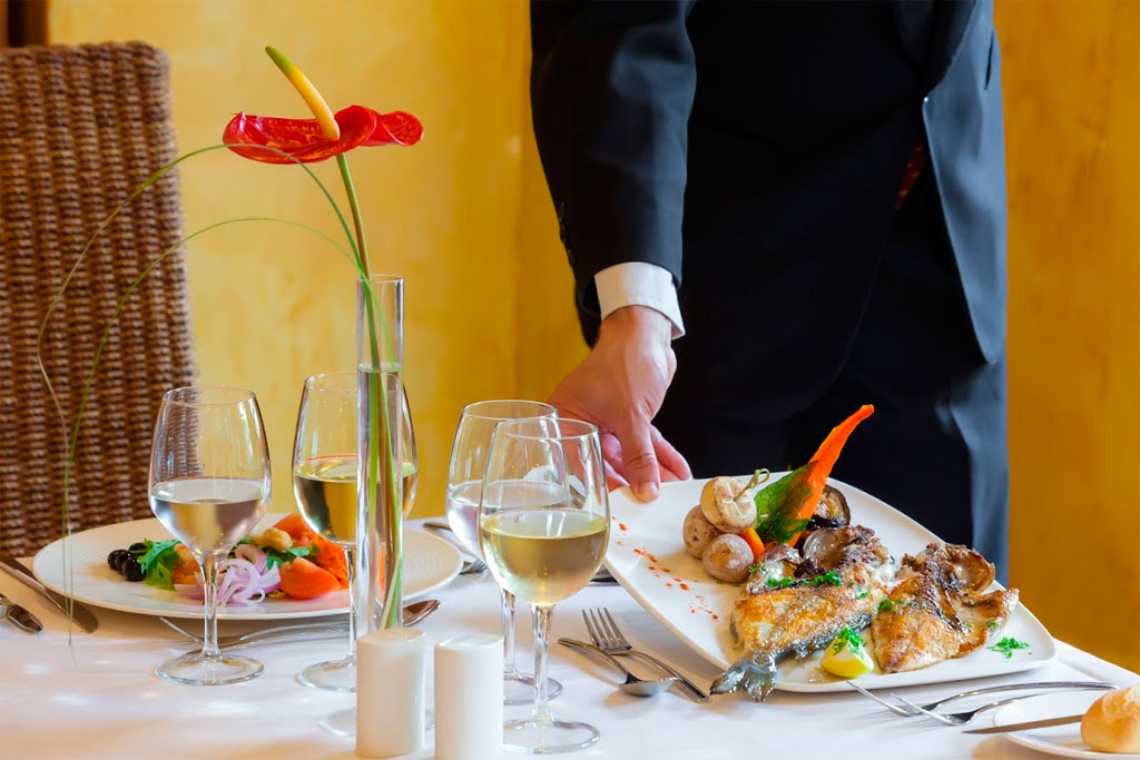 Waiter serving gourmet dishes with wine glasses at a restaurant in Tenerife.