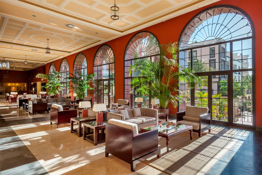 Spacious hotel lounge with armchairs, plants, and large arched windows in Tenerife.