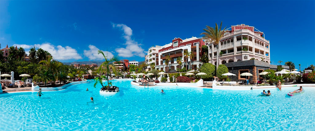 Large pool and resort in Costa Adeje, Tenerife, with people swimming.