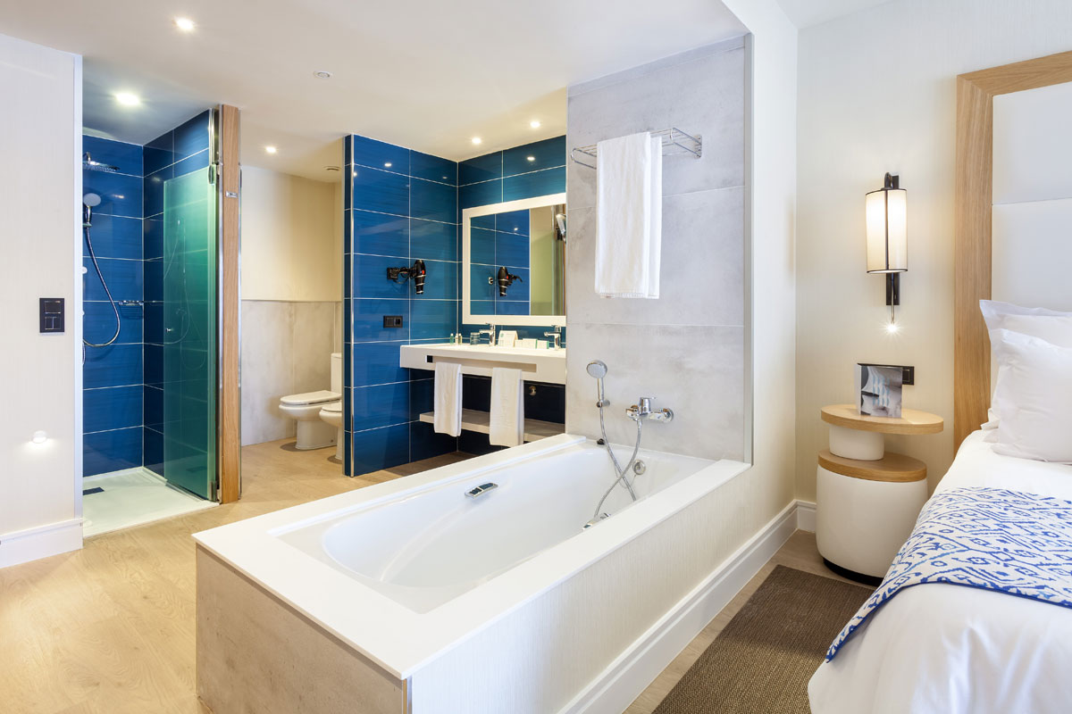Bathroom with blue tiles, bathtub, and bedroom view in a Tenerife hotel.