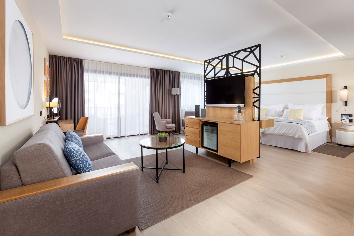 Spacious hotel room in Tenerife with sofa, bed, and TV partition.