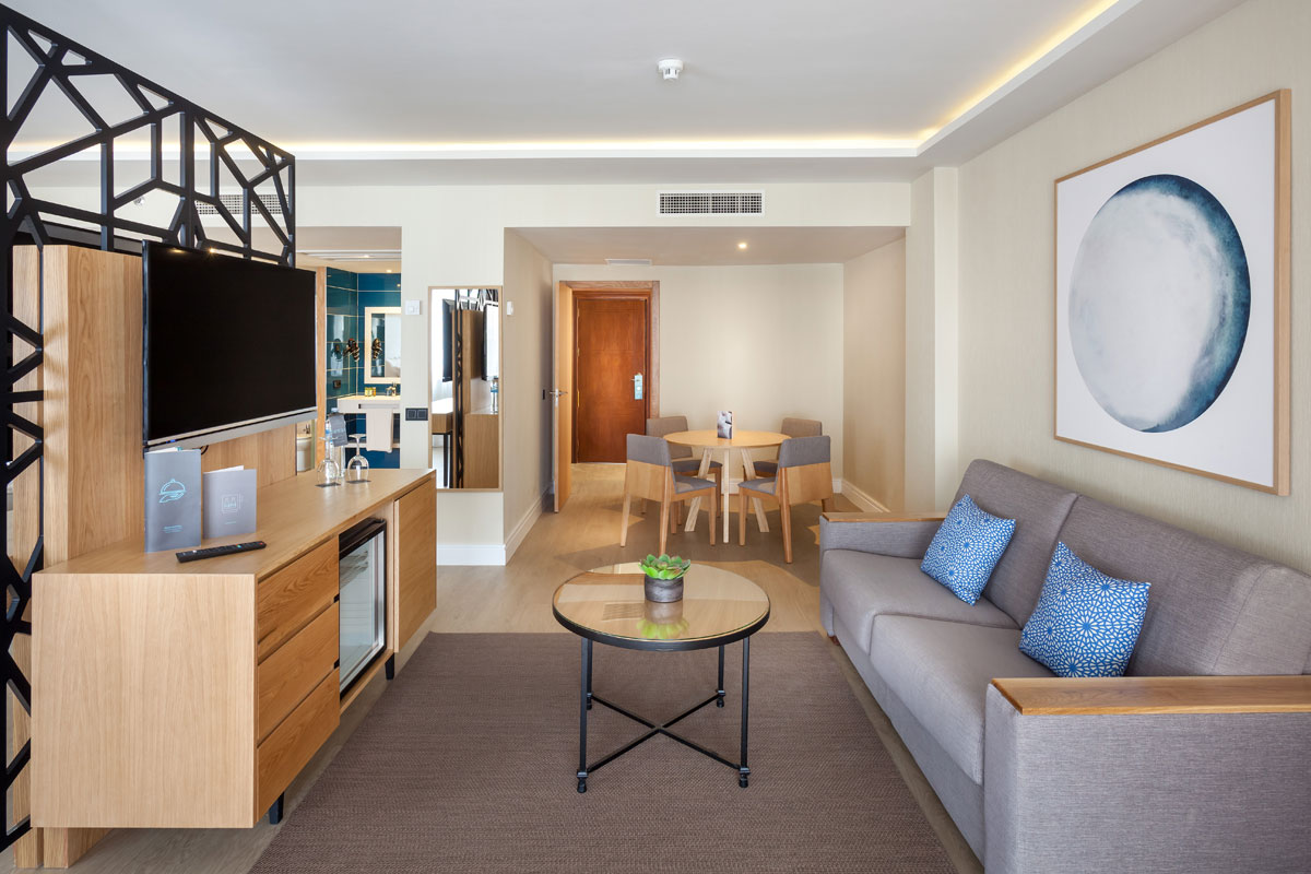 Living room with sofa, TV, round table, and artwork in Tenerife hotel suite.