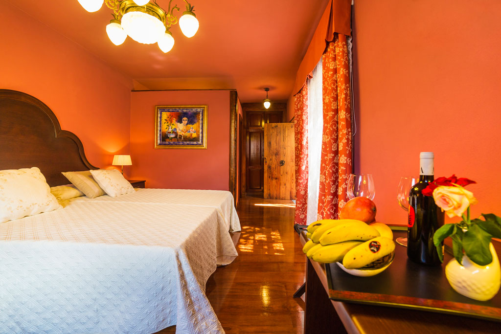 Room with double beds, red walls, fruits, wine, and flowers in Tenerife.